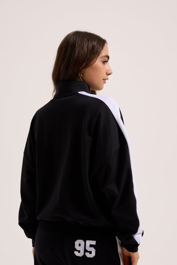 Displays a model wearing the Black 'Juicy' branded college crest track top 