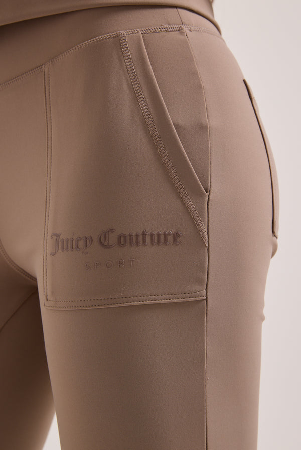 Displays a model wearing the Fungi peached 'Juicy' branded active low rise pants featuring the Juicy Couture branding 