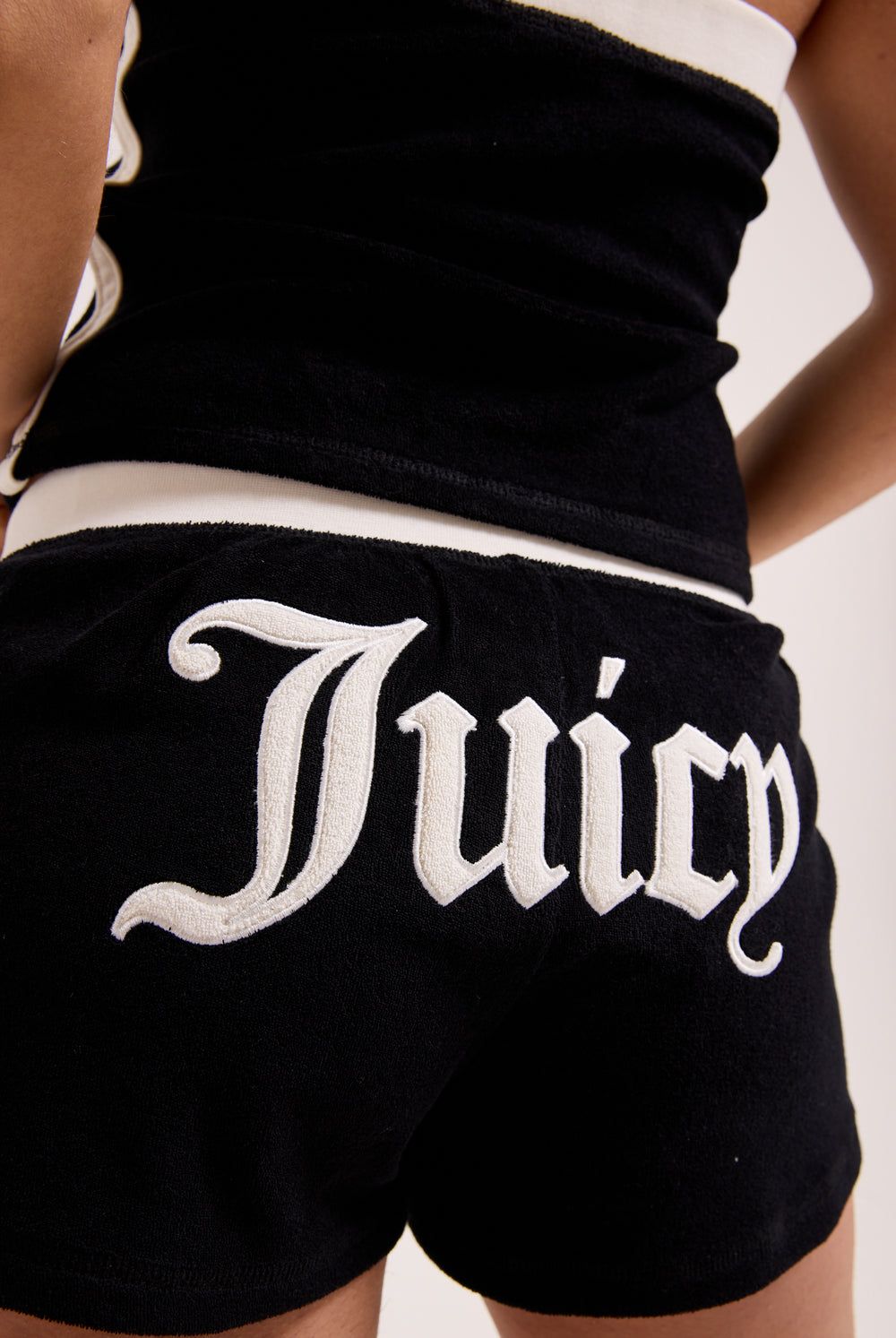 Displays a model wearing the Black Appliqué 'Juicy' branded  Terry booty shorts featuring the juicy branding 