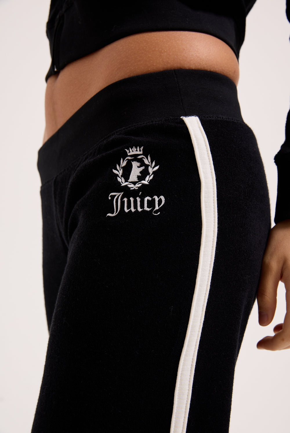 Displays a model wearing the Black appliqué 'Juicy' branded Terry ultra low straight track pants 
