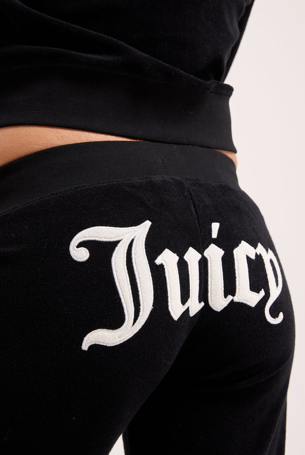 Displays a model wearing the Black appliqué 'Juicy' branded Terry ultra low straight track pants featuring the juicy branding 