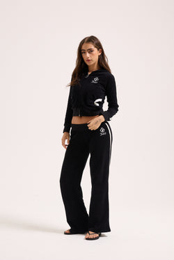 Displays a model wearing the Black appliqué 'Juicy' branded Terry ultra low straight track pants 