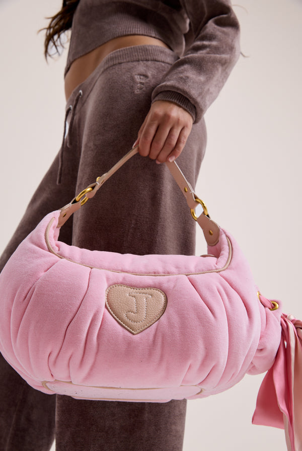 Displays a model holding the Juicy Pink 'Juicy' branded crest velour hobo bag 