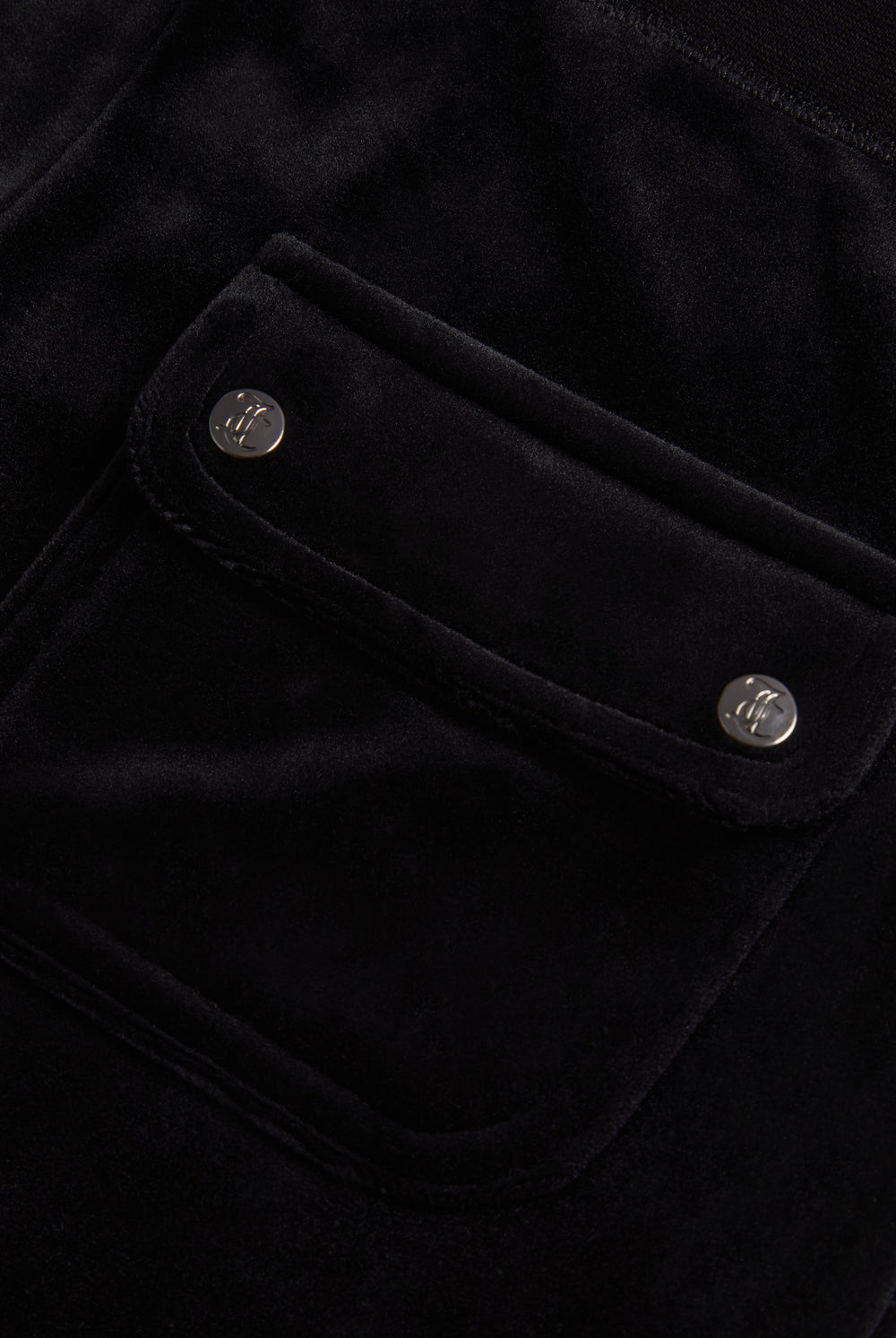 Close-up of the back pocket of black velour bottoms, showing the Juicy Couture branding on the buttons