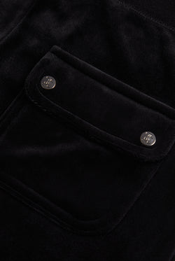 Close-up of the back pocket of black velour bottoms, showing the Juicy Couture branding on the buttons