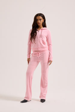 Displays a model wearing the Juicy Pink Classic 'Juicy' branded velour del ray pocketed bottoms