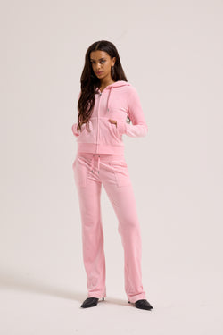 Displays a model wearing the Juicy Pink Classic 'Juicy' branded velour del ray pocketed bottoms