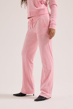 Displays a model wearing the Juicy Pink Classic 'Juicy' branded velour del ray pocketed bottoms