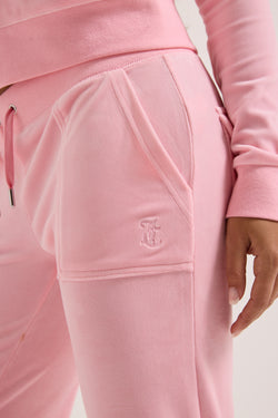 Displays a model wearing the Juicy Pink Classic 'Juicy' branded velour del ray pocketed bottoms