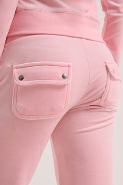 Displays a model wearing the Juicy Pink Classic 'Juicy' branded velour del ray pocketed bottoms