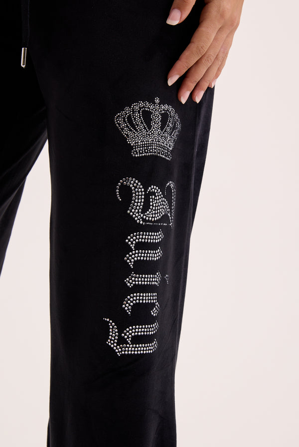Displays a model wearing the black 'juicy' branded diamanté crown OG Straight low rise velour bottoms featuring the juicy branding 