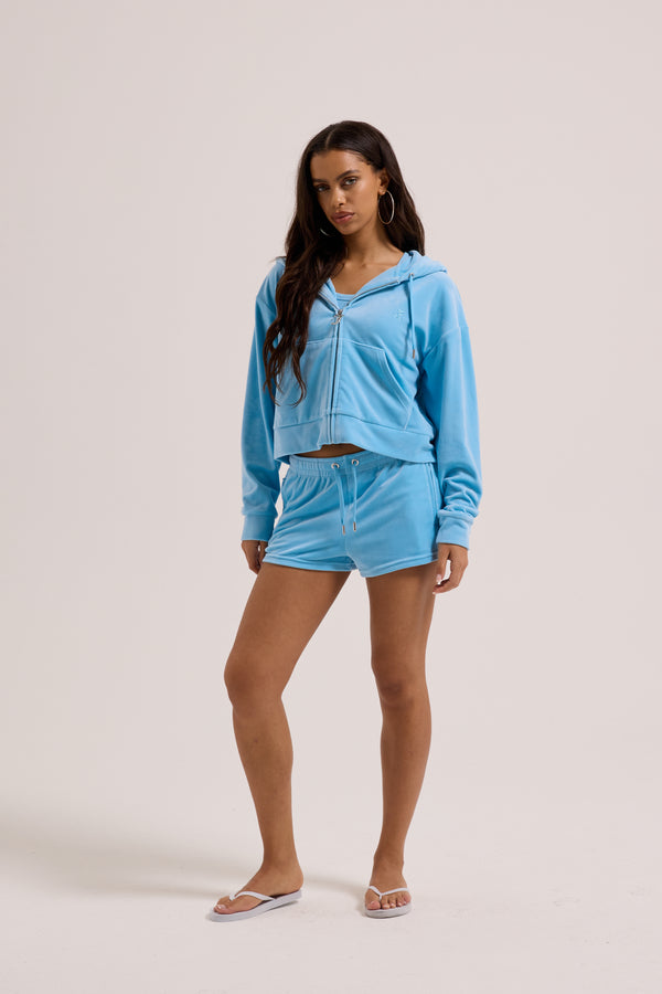 Displays a model wearing the Sky Blue 'juicy' branded Velour outline diamanté track shorts 