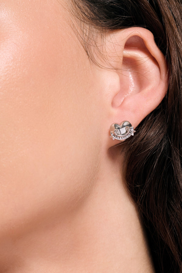 Displays a model wearing the Silver Tone 'Juicy' icon heart stud earrings 