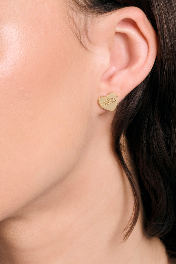 Displays a model wearing the Gold tone 'juicy' branded juicy Couture heart stud earring