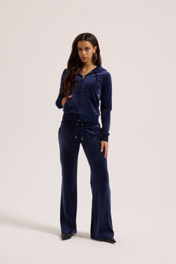 Displays a model wearing the Night Sky 'Juicy' branded low rise velour track pants 