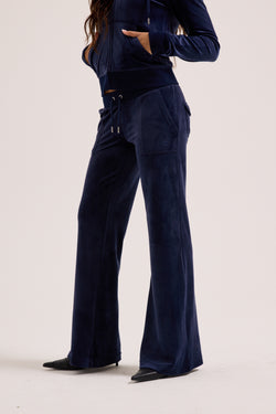 Displays a model wearing the Night Sky 'Juicy' branded low rise velour track pants 