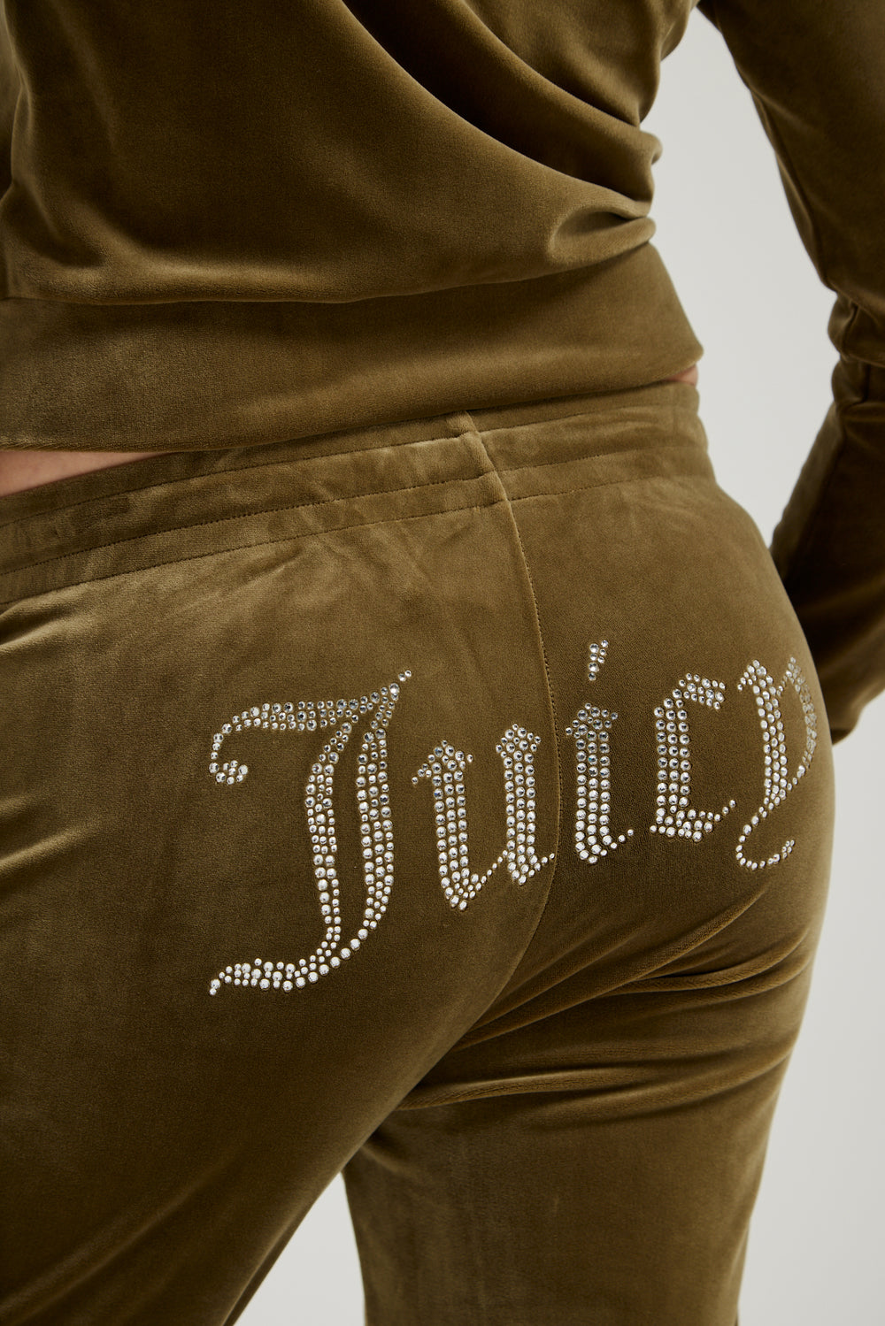 Displays a model wearing the Dark Olive 'Juicy' branded velour diamanté tracksuit bottom