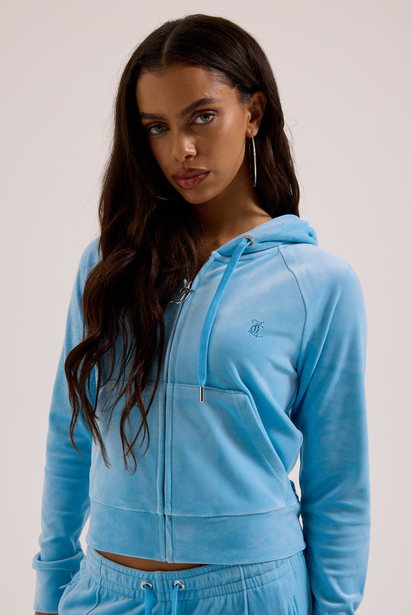 Displays a model wearing the sky blue outline 'juicy' branded velour zip-through hoodie 