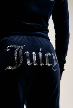 Displays a model wearing the Night Sky 'juicy' branded velour diamanté tracksuit bottom featuring the Juicy logo
