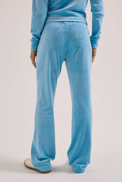 Displays a model wearing the Sky Blue 'Juicy' branded velour outline diamanté tracksuit bottom 
