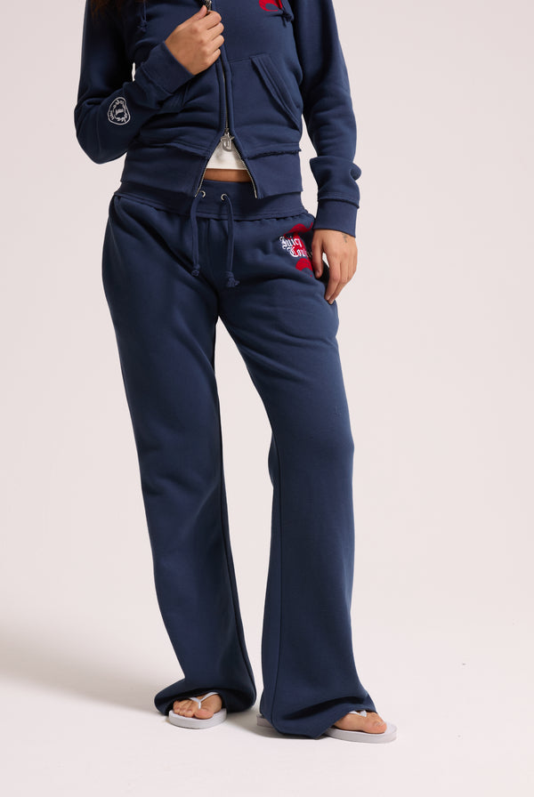 Displays a model wearing the Mood indigo relaxed fit 'juicy' branded flare fleece track pant 