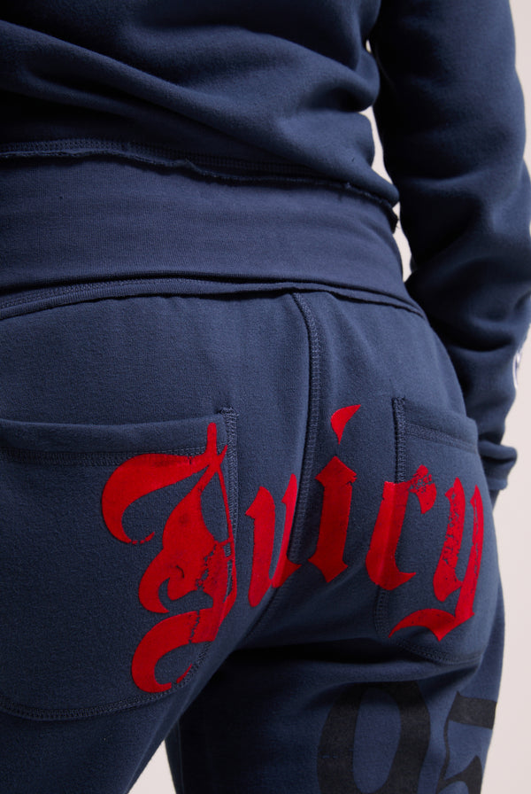 Displays a model wearing the Mood indigo relaxed fit 'juicy' branded flare fleece track pant featuring the juicy branding 