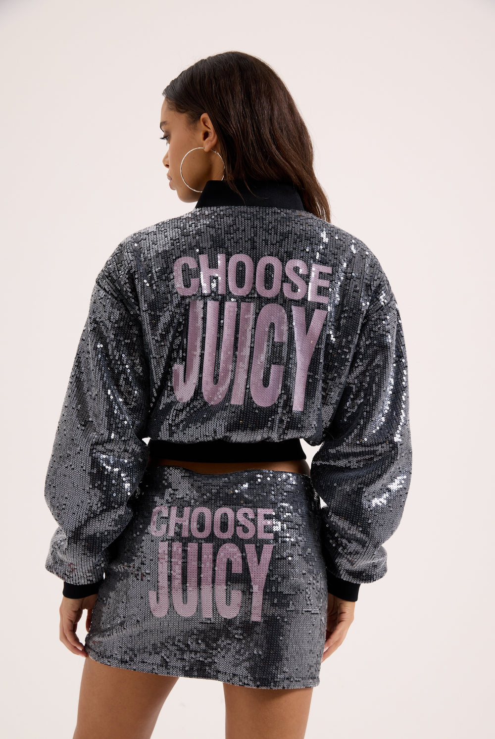 Displays a model wearing the 'juicy' branded choose juicy sequin cropped bomber featuring the juicy branding 