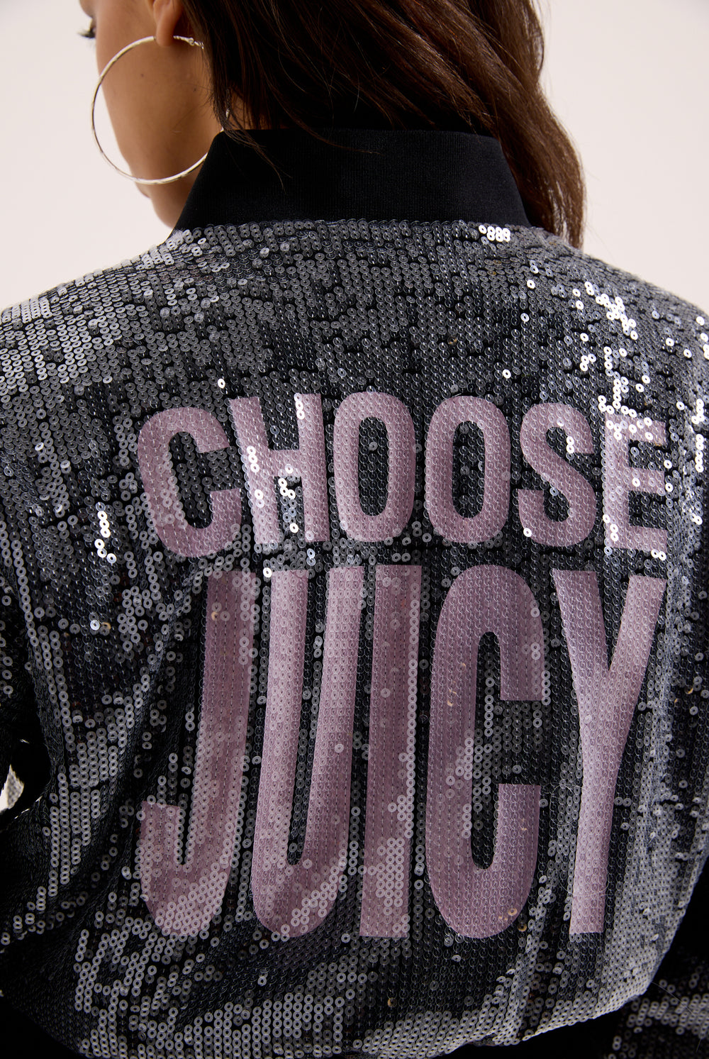 Displays a model wearing the 'juicy' branded choose juicy sequin cropped bomber featuring the juicy branding 