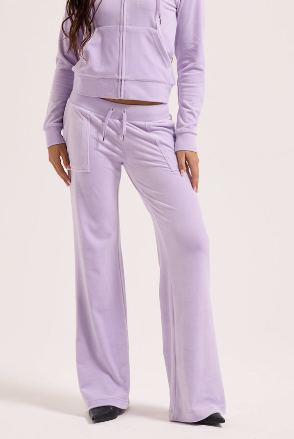 Displays a model wearing the pastel lilac 'juicy' branded low rise flare classic velour track pant 