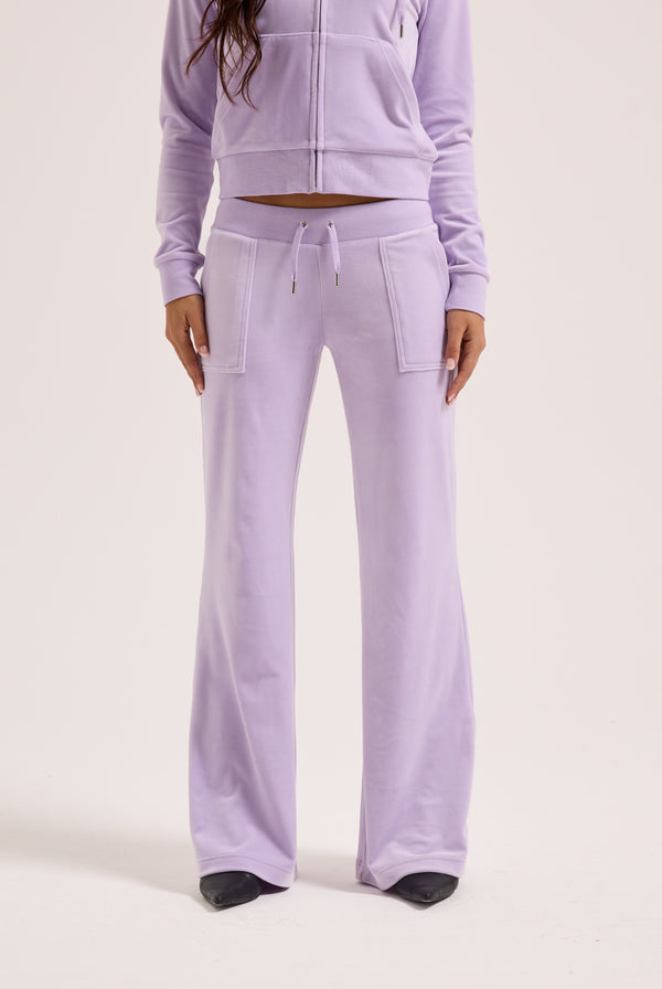 Displays a model wearing the pastel lilac 'juicy' branded low rise flare classic velour track pant 