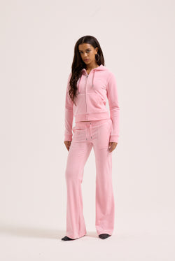 Displays a model wearing the Juicy Pink 'Juicy' branded low rise flare classic velour track pant 