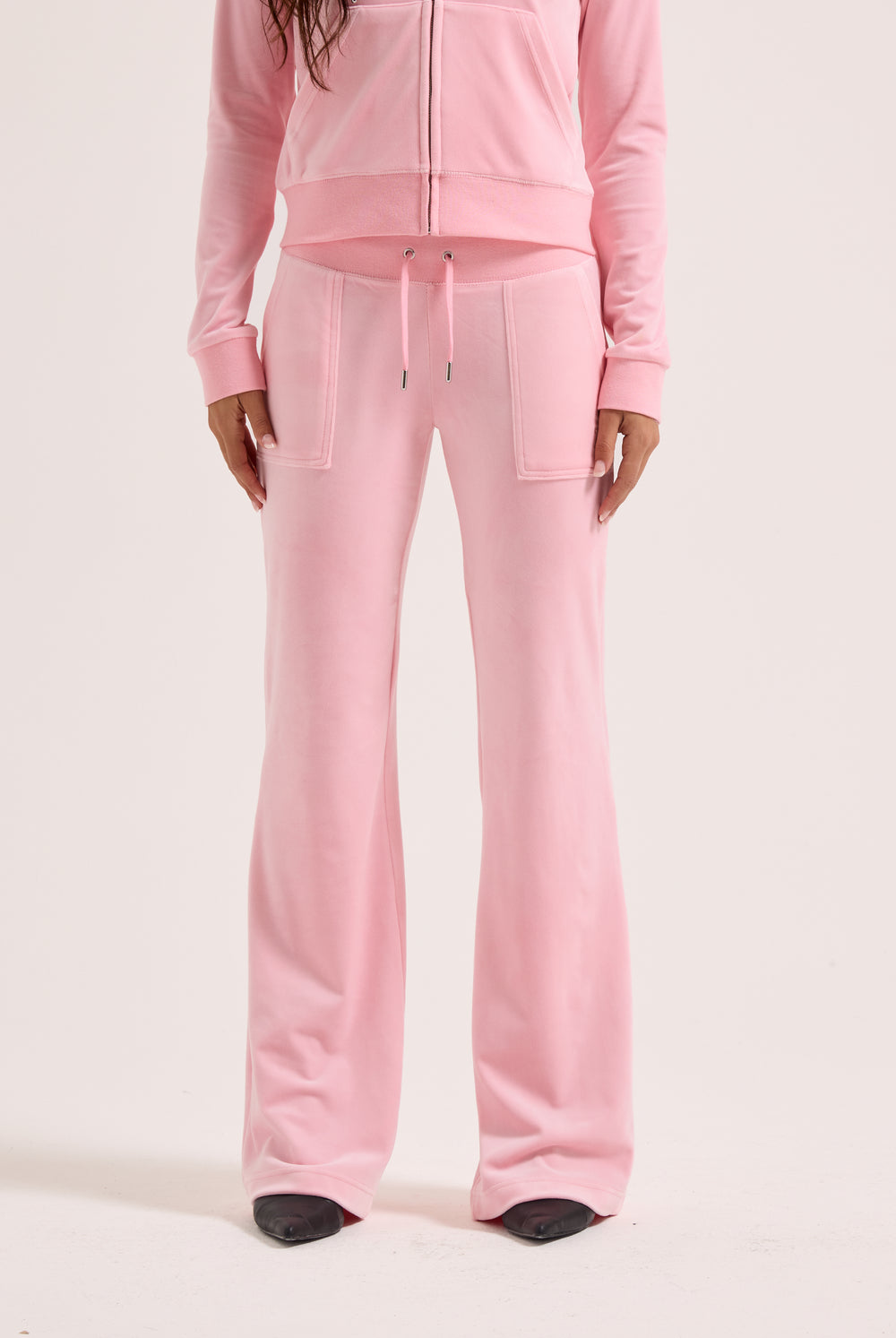 Displays a model wearing the Juicy Pink 'Juicy' branded low rise flare classic velour track pant 