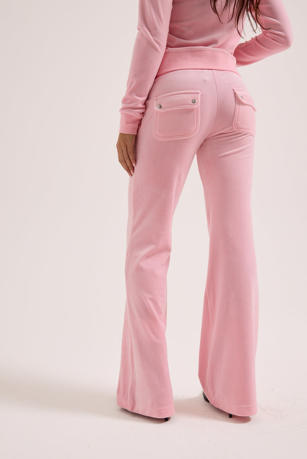 Displays a model wearing the Juicy Pink 'Juicy' branded low rise flare classic velour track pant 
