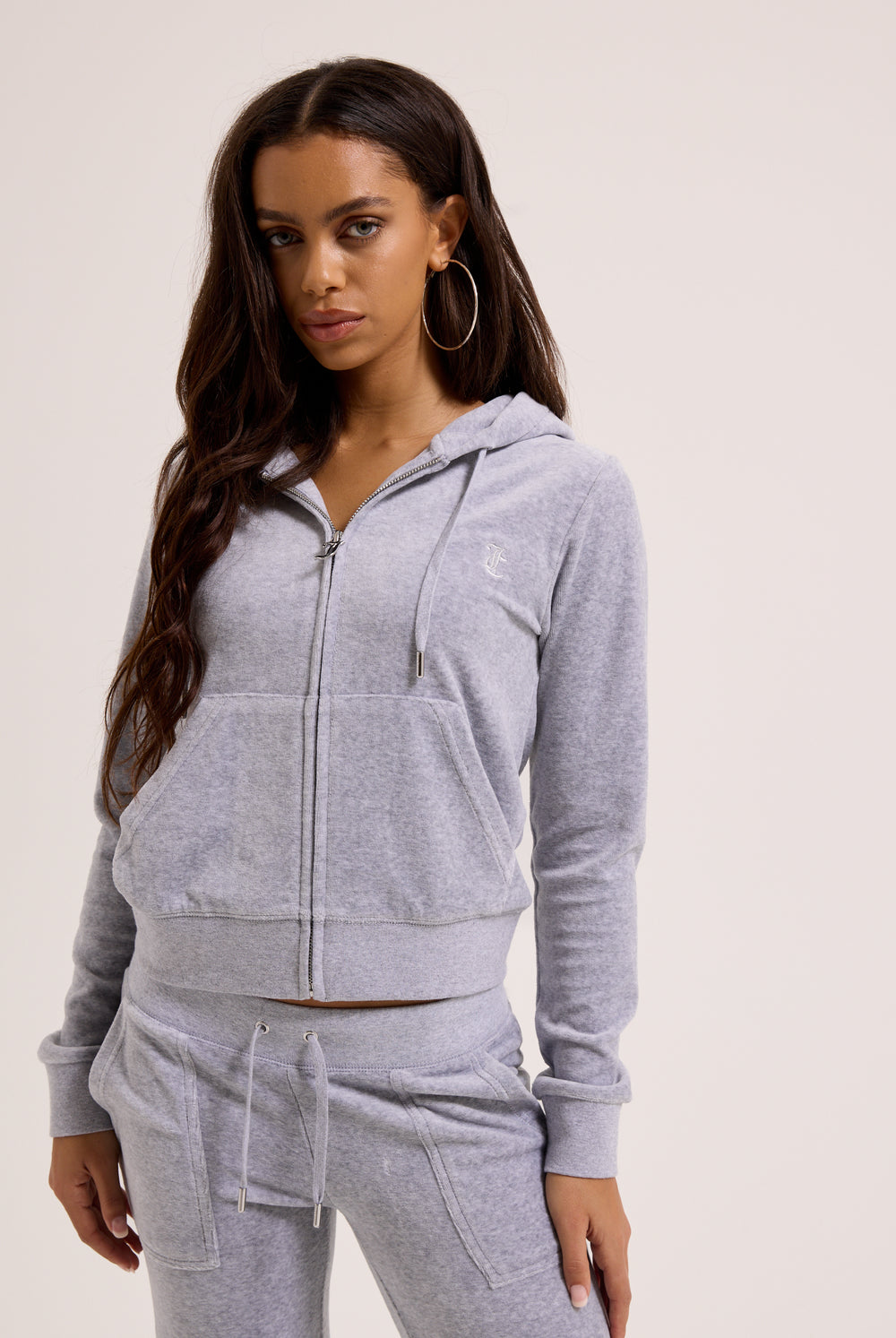 Woman wearing a gray zip-up hoodie and matching pants on a plain background