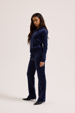 Woman wearing a navy blue velour tracksuit on a white background
