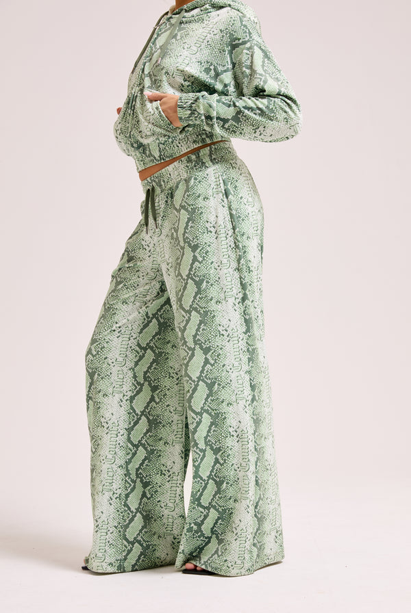 Displays a model wearing the green snake print 'Juicy' branded diamanté low rise track bottom 