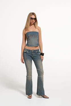 Displays a model wearing the Mid Wash 'Juicy' branded Sand Denim Studded Corset Top