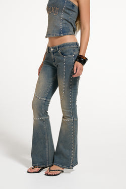 Displays a model wearing the Mid Wash 'Juicy' branded Sand Stud Moto Bootcut Jeans