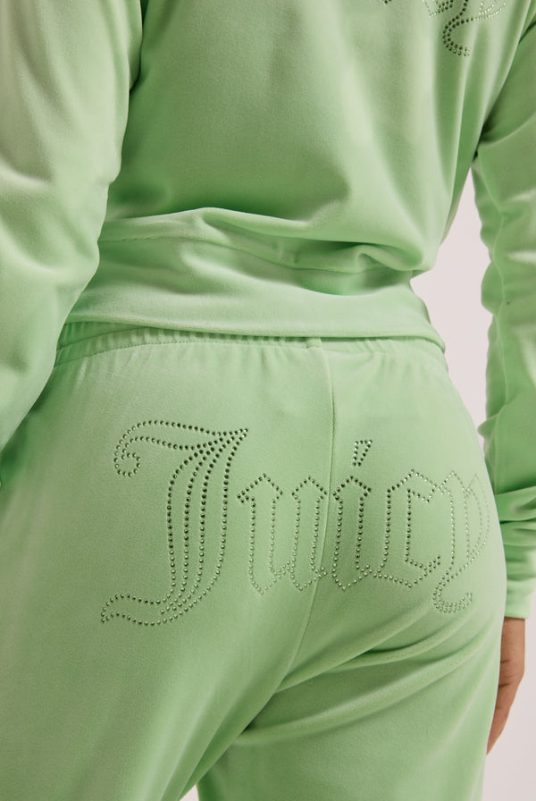 Displays a model wearing the pistachio green outline 'Juicy' branded velour diamanté tracksuit bottom featuring the juicy branding 