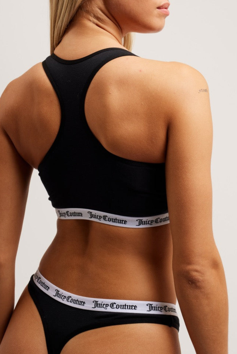 Displays a model wearing the Black 'juicy' branded cotton bralette