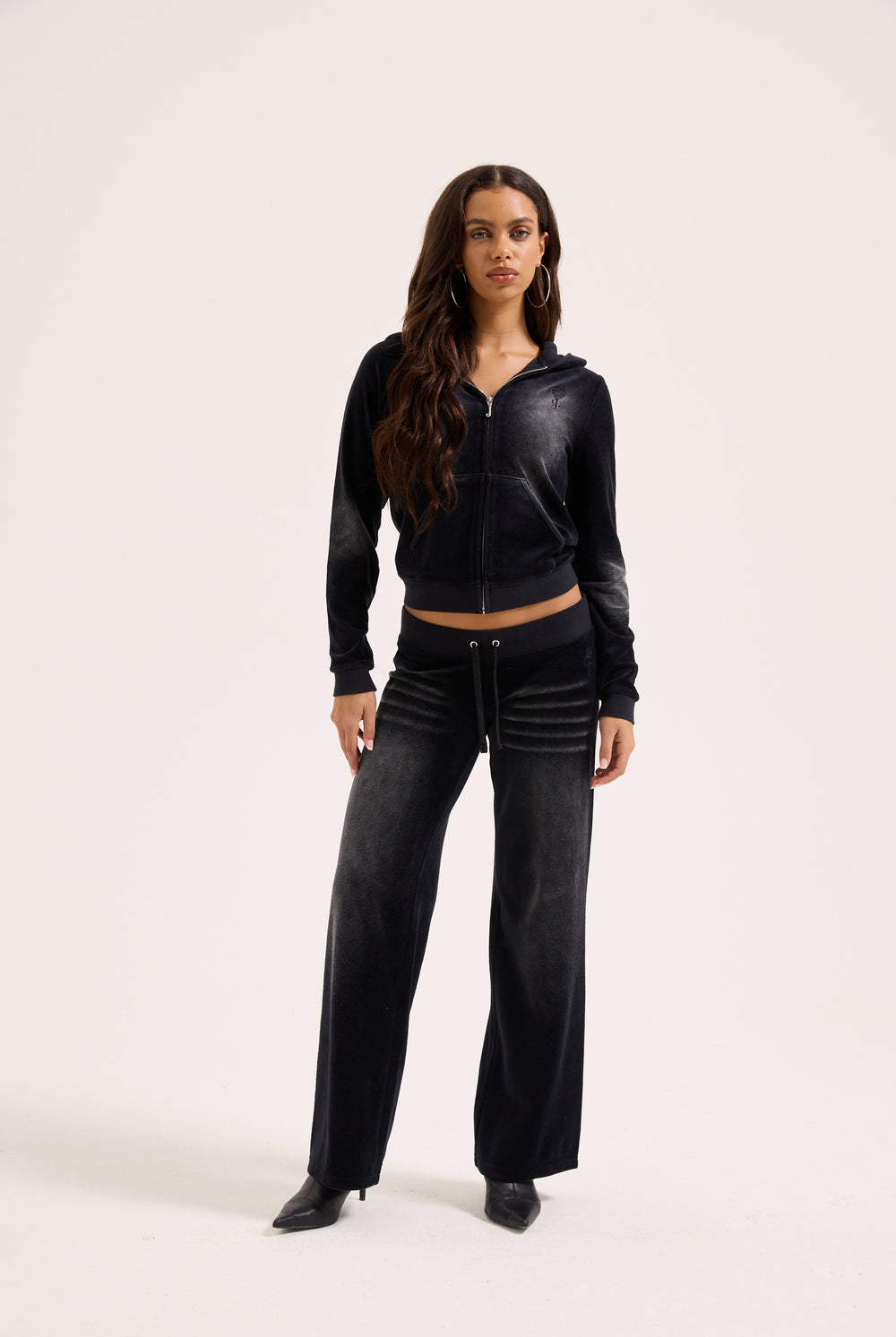 Displays a model wearing the washed black cotton 'Juicy' branded velour og straight low rise pants 