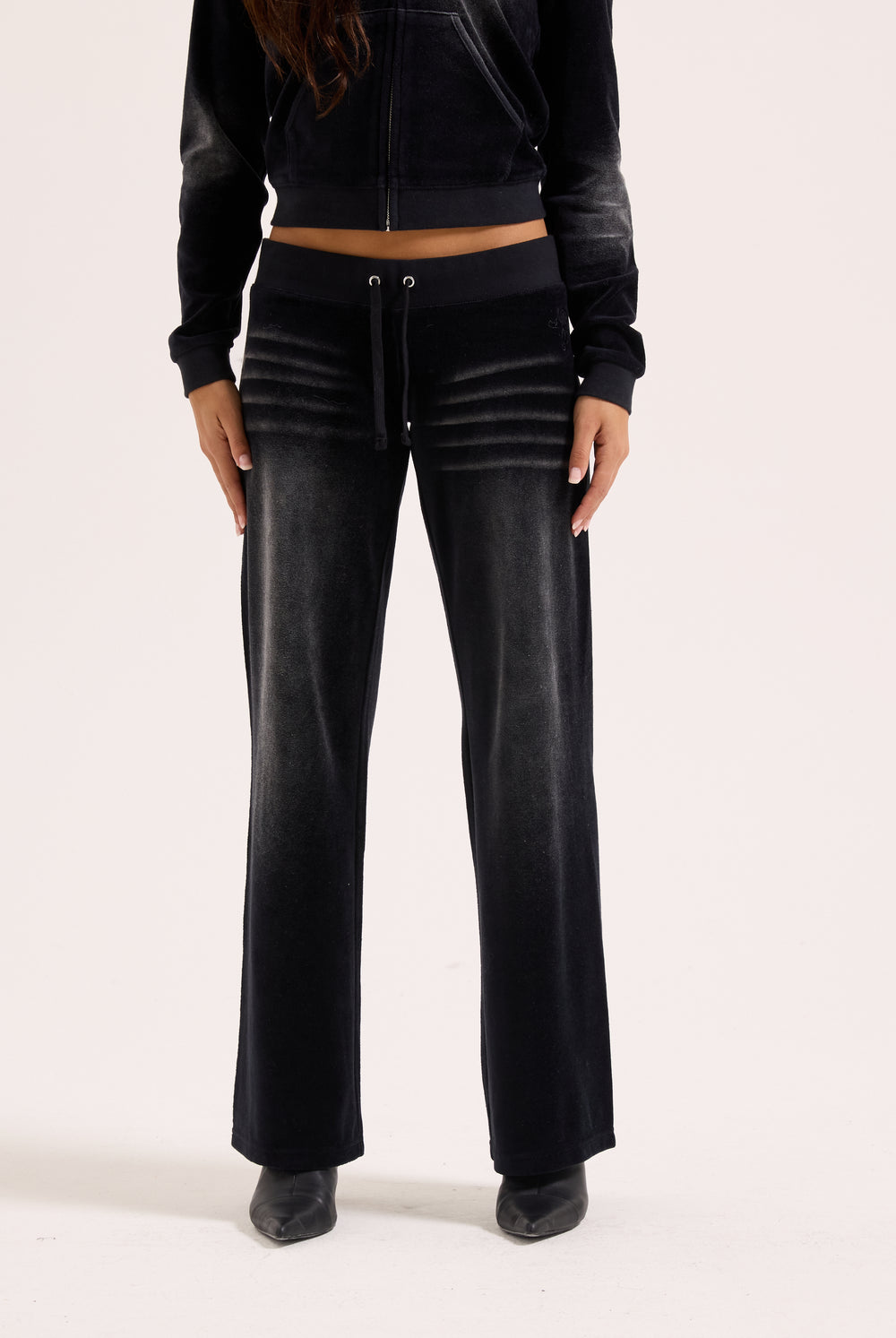 Displays a model wearing the washed black cotton 'Juicy' branded velour og straight low rise pants 