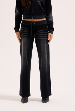 Displays a model wearing the washed black cotton 'Juicy' branded velour og straight low rise pants 