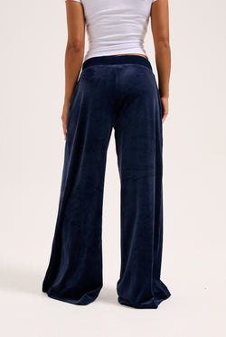 Displays a model wearing the night sky 'juicy' branded Sky Wide leg classic velour track pant 
