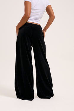 Display a model wearing the Black 'Juicy' branded wide leg classic velour track pant 